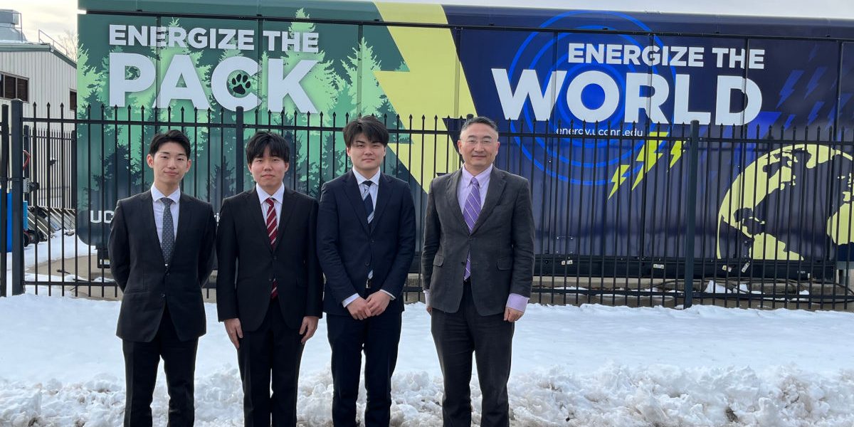 Visitors from Kyushu University standing in front of fuel cell dressed in black suits